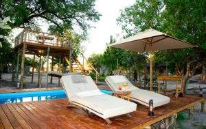 two lounge chairs and an umbrella next to a pool at Candies Vacation Cottage Khwai in Khwai