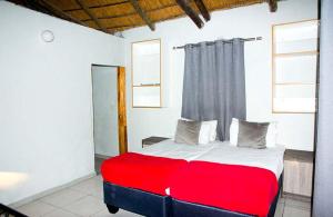 a bedroom with a red and white bed with two windows at Candies Vacation Cottage Khwai in Khwai