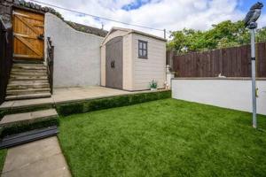 a backyard with a small shed in the grass at Heritage Cottage by StayStaycations in Pontypridd