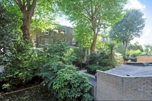 a garden with trees and a brick wall and a building at Bright & Spacious West London Apartment in London