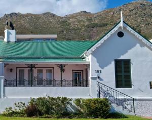 a white house with a green roof and mountains in the background at Milkwood Cottage, Beachfront family vacation home, Sleeps 6 in Gordonʼs Bay