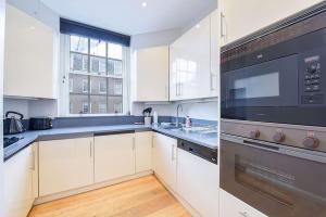 een keuken met witte kasten en een zwart apparaat bij 2 Bedroom Apartment- Mayfair (4) in Londen