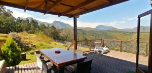 een houten terras met een tafel en stoelen en bergen bij Summer Villa in Mosselbaai
