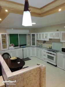 a kitchen with white cabinets and a table in it at شقة مفروشة سكنية في مرج الحمام in Amman