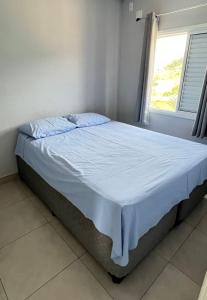 Bett in einem weißen Zimmer mit Fenster in der Unterkunft Apto novo com piscina em Ubatuba - Praia Maranduba in Ubatuba