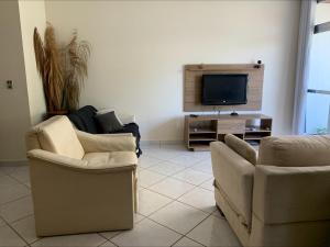 a living room with two chairs and a flat screen tv at Apartamento no Guarujá para 8 pessoas in Guarujá