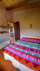 Un dormitorio con una cama con una manta de colores. en MAMAICUNA CABAÑA en Tilcara