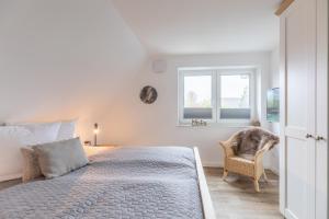 a white bedroom with a bed and a chair at Getidenhus Emma in Sankt Peter-Ording