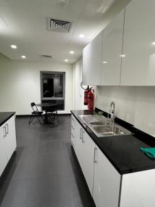 uma cozinha com armários brancos, um lavatório e uma mesa em Lodges em Al Ain