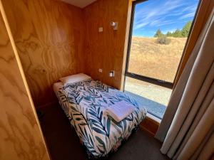a small bedroom with a bed and a window at The Red Nest - Lake Tekapo in Lake Tekapo