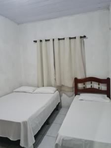 two beds in a white room with curtains at Casapraiacururupe in Ilhéus
