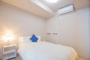 a white bedroom with a white bed with a blue pillow at shirokane apartment Vx in Tokyo