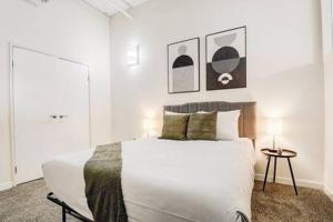 a white bedroom with a bed and two pictures on the wall at CozySuites - 2BR with Direct Skybridge Access #5 in Indianapolis