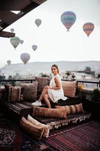 Uma mulher de vestido branco sentada num sofá com balões de ar quente. em Royal Stone Houses - Goreme em Goreme