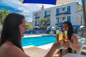 two women sitting next to a pool with drinks at Hotel Miami en Melgar in Melgar
