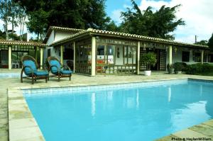 a swimming pool with two chairs and a house at Hotel Fazenda Ceu Aberto in Gravatá