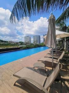a group of lounge chairs with an umbrella and a pool at Family Fun Staycation @ Thelima Suite in Kajang