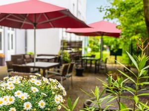 eine Terrasse mit Tischen, Stühlen, Sonnenschirmen und Blumen in der Unterkunft ibis Hotel Regensburg City in Regensburg