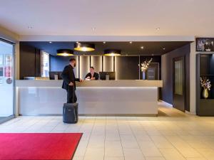 a man with a suitcase standing in front of a counter at Mercure Hotel Duisburg City in Duisburg