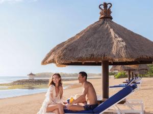 a man and woman sitting on the beach under an umbrella at Sofitel Bali Nusa Dua Beach Resort in Nusa Dua