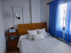 a bedroom with a white bed with blue curtains and a window at Luz de la Bahía II - Bahía Sur - Cádiz in San Fernando