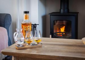 a bottle of whiskey and three wine glasses on a table with a fireplace at Jasmine Cottage, sleeps 6 near Elie, with garden in Fife