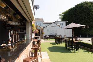 un patio con mesas, sillas y una sombrilla en The Dog in Over Peover, en Knutsford