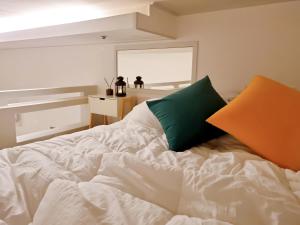 ein weißes Bett mit einem orangen und grünen Kissen darauf in der Unterkunft Yellow House - Duplex, Night view, White modern interior in Bucheon