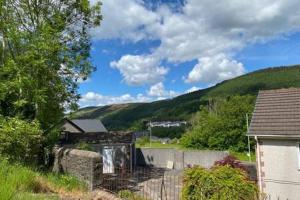 a house in a field with a mountain in the background at Taff Valley Heartwarming Cottage In Aberafan Merthyr Tydfil By STAE-Homes in Merthyr Tydfil