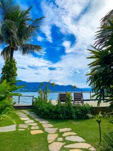 two benches and a palm tree next to the ocean at Pousada Vila das Velas in Ilhabela