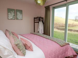Schlafzimmer mit einem Bett mit rosa Bettwäsche und einem Fenster in der Unterkunft Dol Blodau in Llandrindod Wells