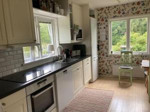 a kitchen with white cabinets and a sink and two windows at Stuga i Norra Kvarnviken in Bengtsfors +1 photo