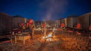 un hombre sentado frente a un fuego por la noche en Nomad Camp, en Erfoud