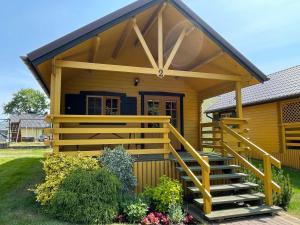 una pequeña casa amarilla con porche y escaleras en Domki i pokoje "ZIELONA PRZYSTAŃ", en Sztutowo