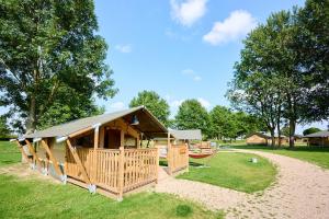 a large wooden cabin with a roof on a grass field at Glamping Betuwe in Kesteren