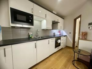 cocina con armarios blancos y encimera negra en Modern 1 Bedroom self contained apartment en Welwyn Garden City