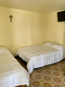 two beds in a room with a cross on the wall at Hostal Las Quince Letras in Tehuacán