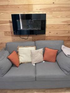 eine graue Couch mit Kissen drauf mit Fernseher in der Unterkunft L’Eden Studio Suite Balneo plein centre d’Andernos in Andernos-les-Bains