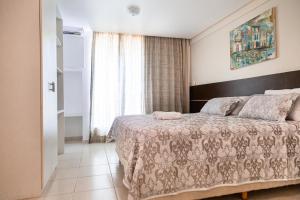a bedroom with a bed with a blanket and a window at Athenas Suites By BnbHost in Salvador