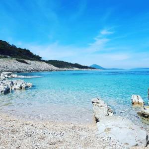 a beach with blue water and rocks on the shore at Apartman RUBY in Mali Lošinj