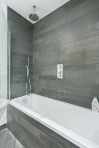 a white bath tub in a bathroom with gray tiles at The Vale - Luxury Apartments in London