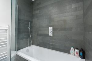 a bathroom with a white tub and a gray tile wall at The Vale - Luxury Apartments in London