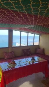 a room with a bed with a table and windows at Suerte Loca in Sidi Ifni