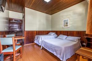 a bedroom with two beds and a table and a desk at Pousada Saint Gallen in Campos do Jordão