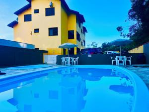 a pool in front of a building with chairs and umbrellas at Apartamento Mar Brasil II in Ubatuba