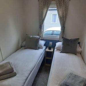 twee bedden in een kleine kamer met een raam bij Emi's Caravan in Port Seton