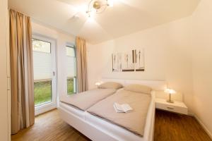 a white bedroom with a bed and a window at Dünenresort Binz - Ferienwohnung 4.1.6 in Binz