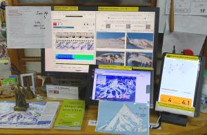 einen Schreibtisch mit einem Computermonitor und mehreren Papieren in der Unterkunft Hakuba Ski-Kan in Hakuba