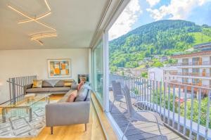 ein Wohnzimmer mit einem Balkon mit einem Sofa und Stühlen in der Unterkunft Penthouse Ari - by Alpen Apartments in Zell am See