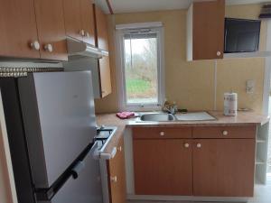 a kitchen with a white refrigerator and a sink at Mobilhome Côté Haie in Holque
